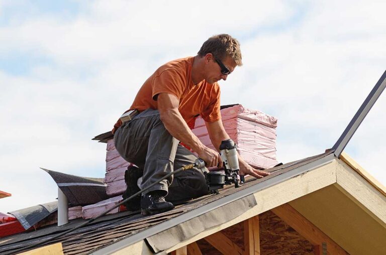 An insurance adjuster examines damaged shingles on a residential roof after a storm.