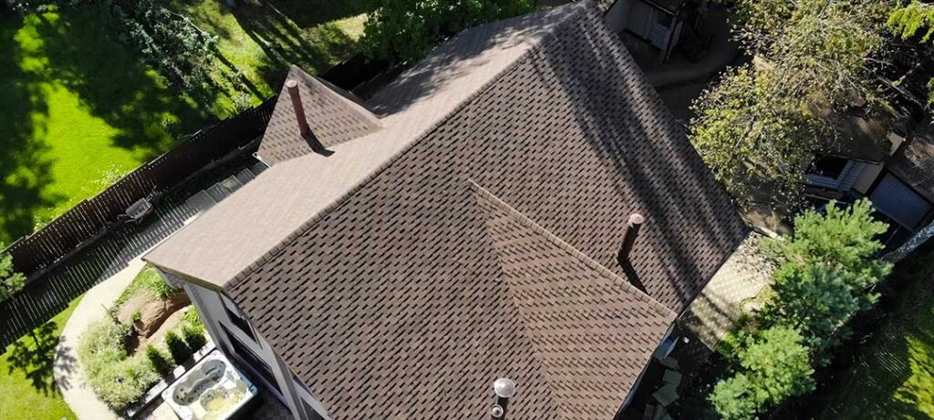 Snow, windblown leaves, and lifted shingles on a residential roof after changing weather.