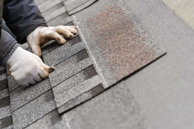 Homeowner examining roof shingles with binoculars while standing beside a house.